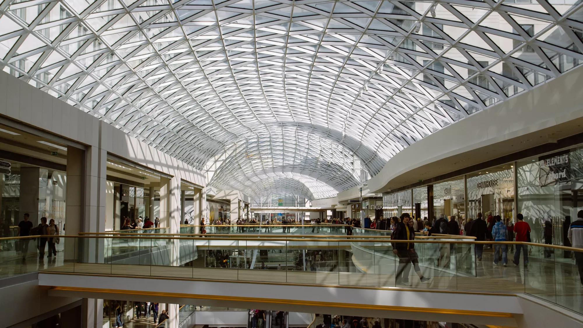 large multi-level shopping mall with various stores, escalators, and visible security measures, including a retail alarm system in place to protect the premises