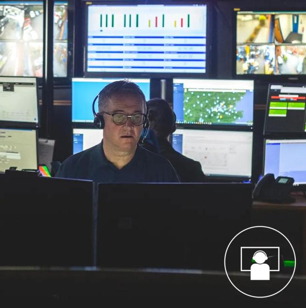 säkerhetsvakt som besvarar ett anrop i en övervakningscentral med flera videoövervakningsskärmar som visar säkerhetsdata